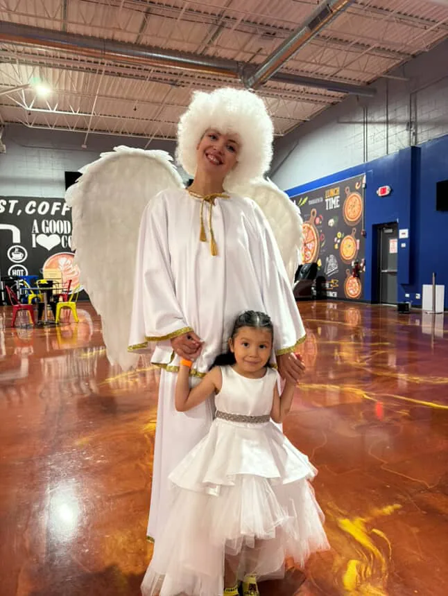 Angel-costumed entertainer holding hands with a child at an event