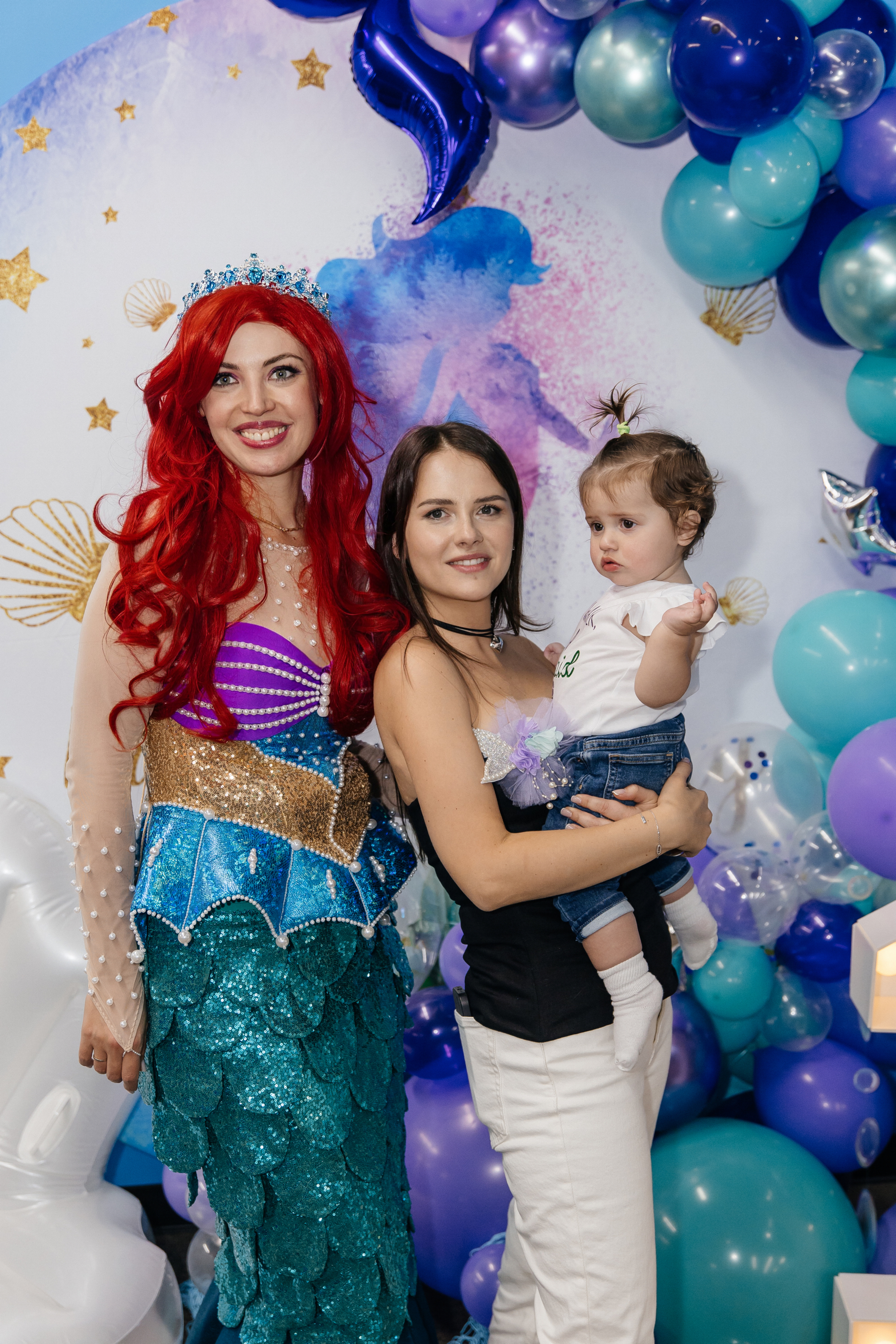 Mermaid entertainer posing with a mom and child at a themed celebration