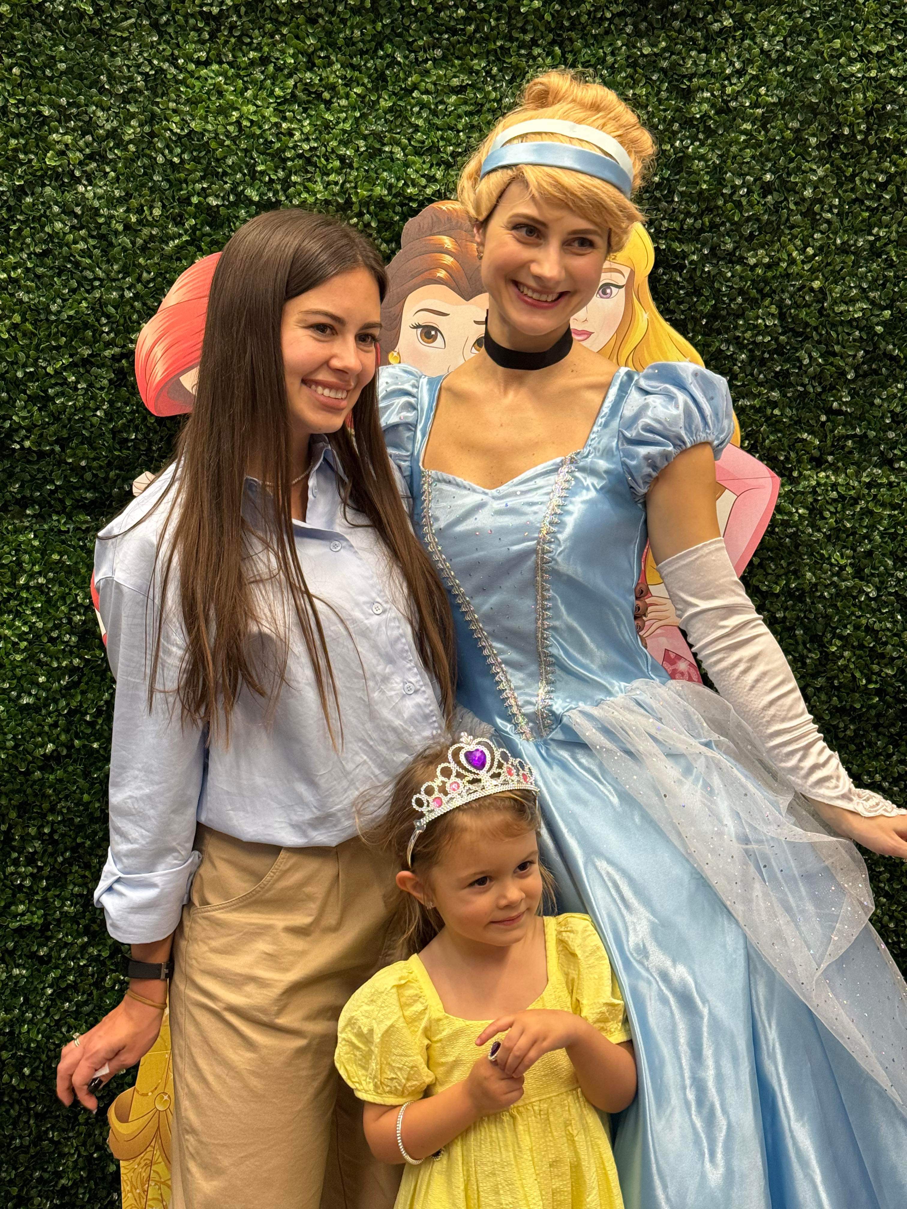 Cinderella entertainer smiling with a young girl and her parent at a party backdrop